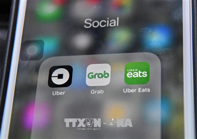 Ứng dụng Grab (giữa) và Uber (trái) trên điện thoại di động. Ảnh: AFP/TTXVN